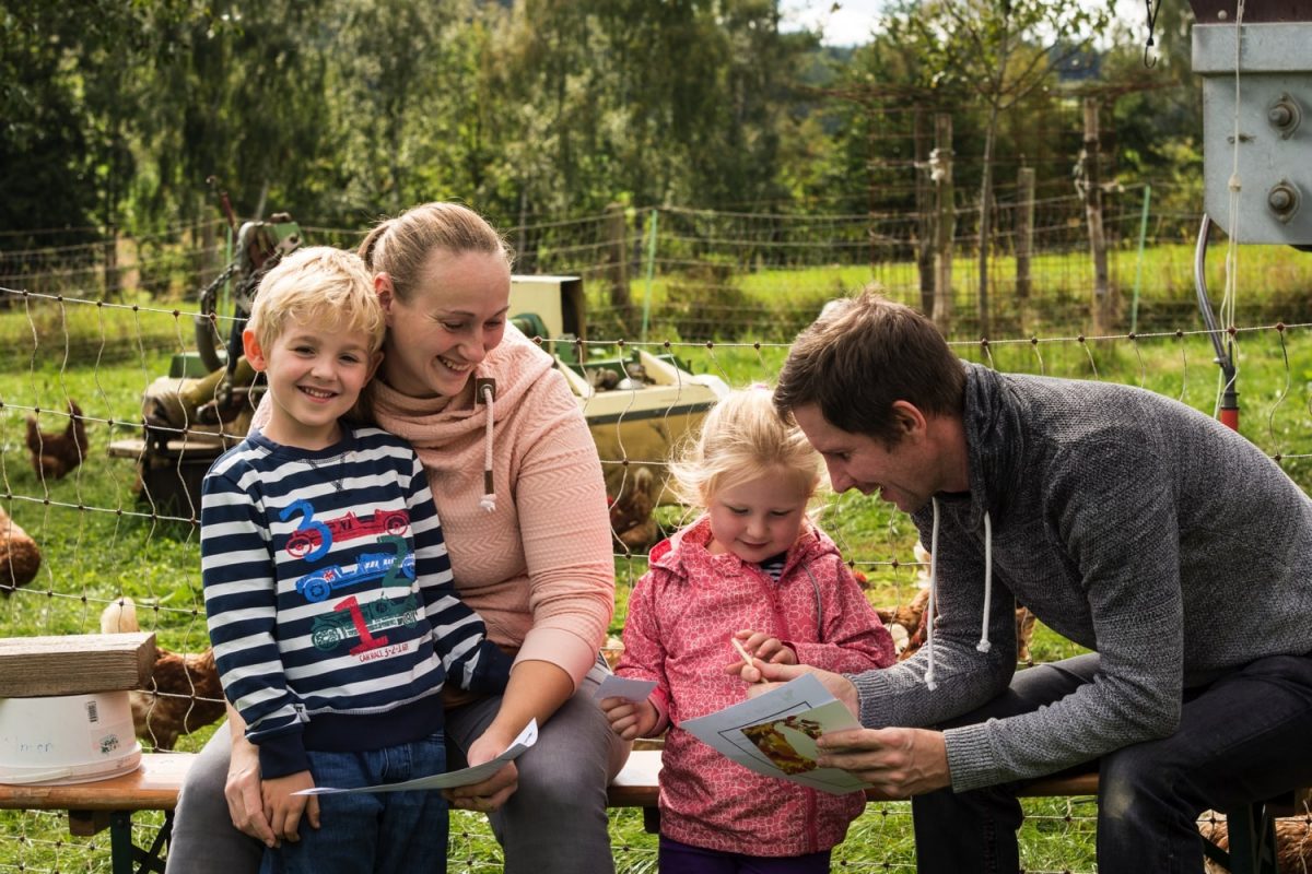 Familie sitzt in einem Garten mit Hühnern